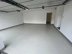 Leere Garage mit fugenlosem, hellgrauem und fein gesprenkeltem Boden und geöffnetem Sektionaltor